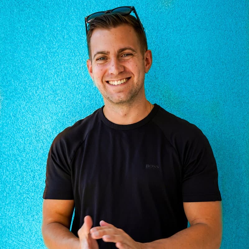 Rob Brautigam, smiling, in a black T-shirt against a teal wall