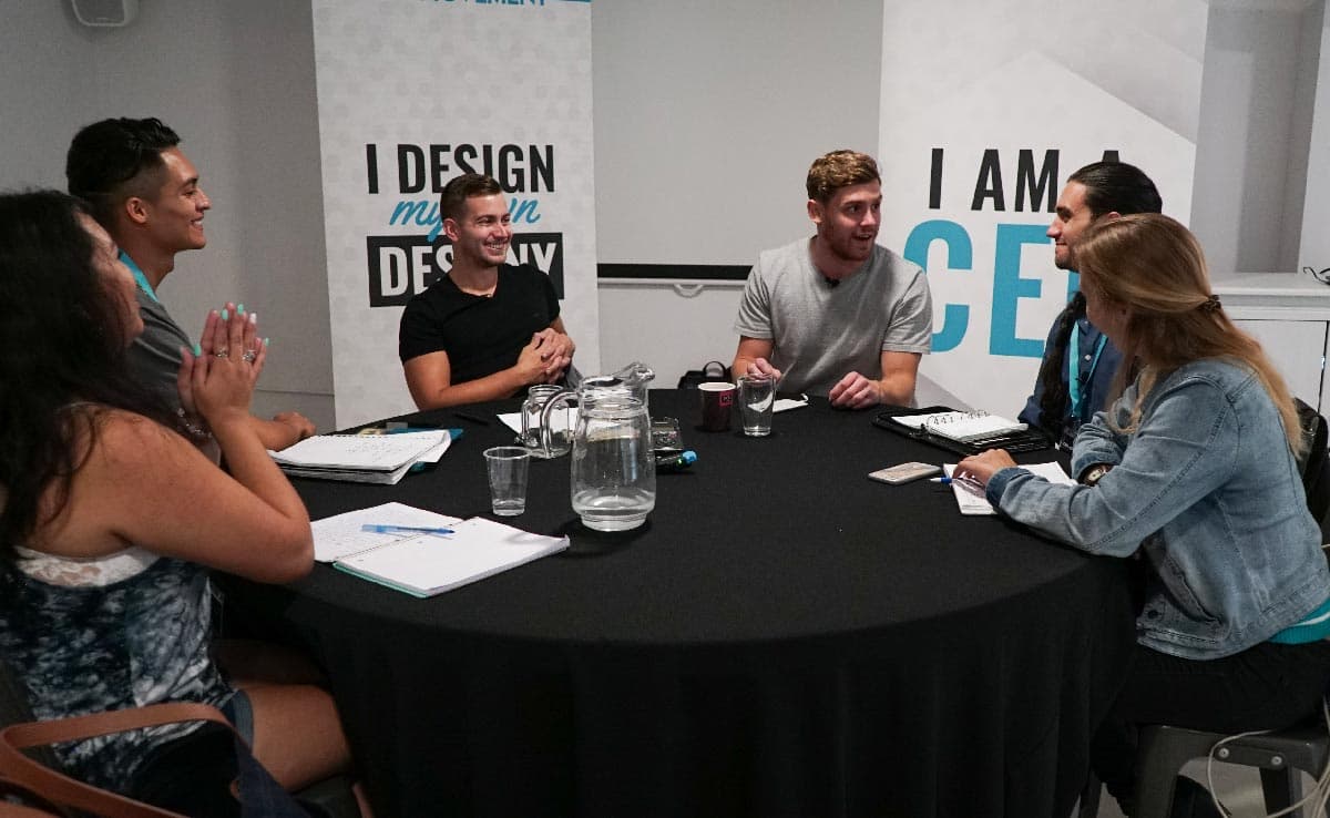 A working roundtable, notebooks open, in front of an 'I am a CEO' banner