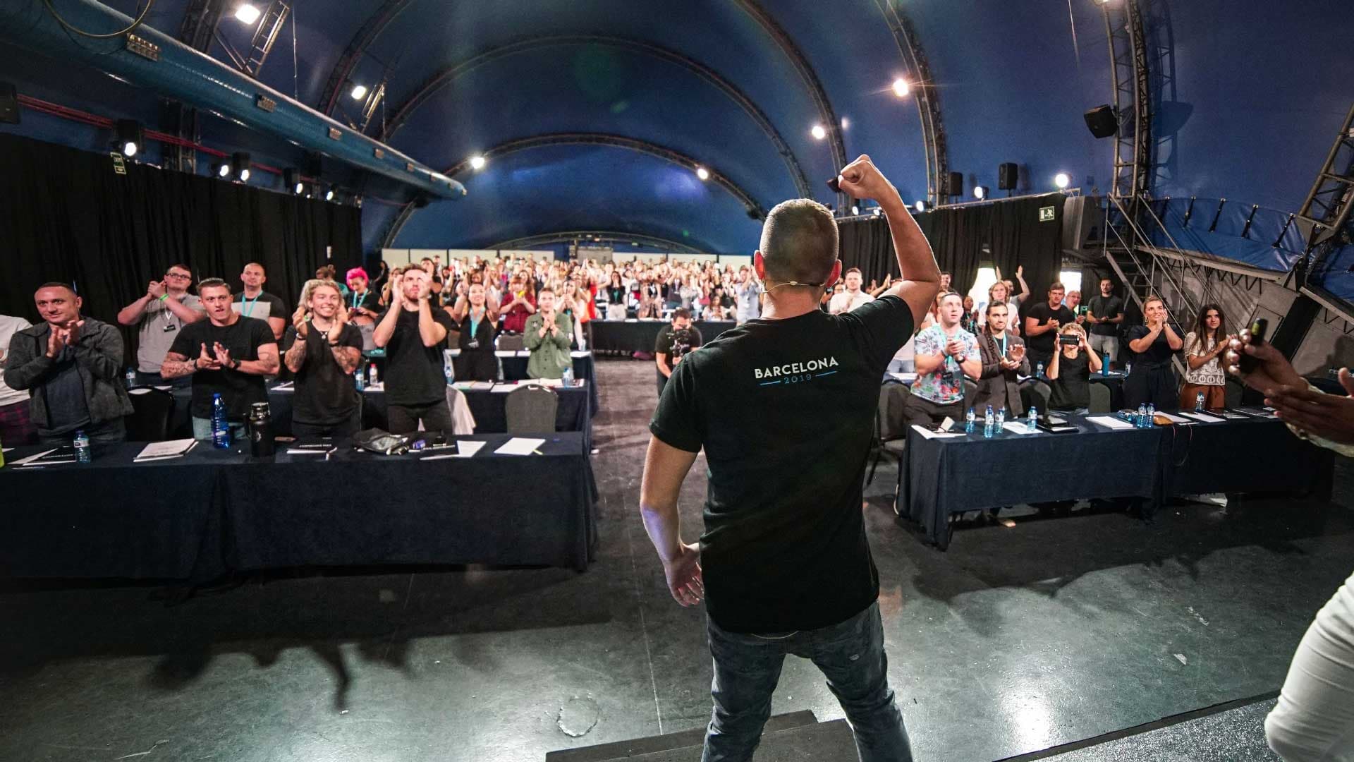 Rob Brautigam on stage, seen from behind with his fist raised, as a full room stands and applauds
